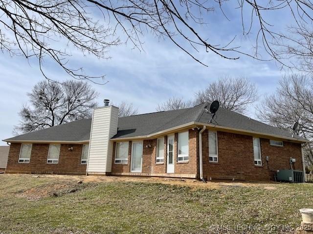 back of property featuring a yard, brick siding, central AC, and a chimney