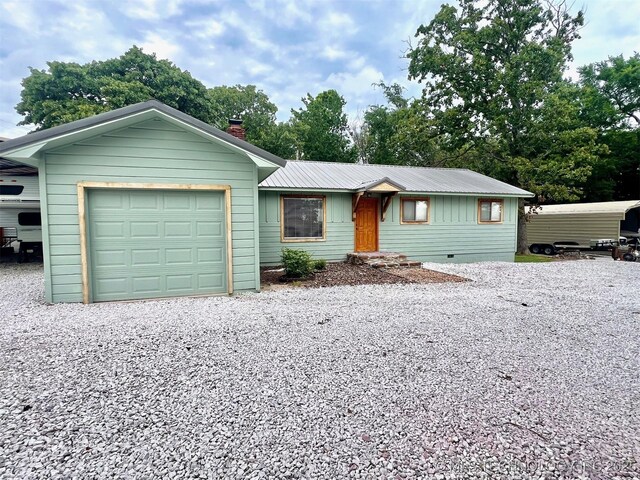 ranch-style house featuring an attached garage, metal roof, driveway, and a chimney