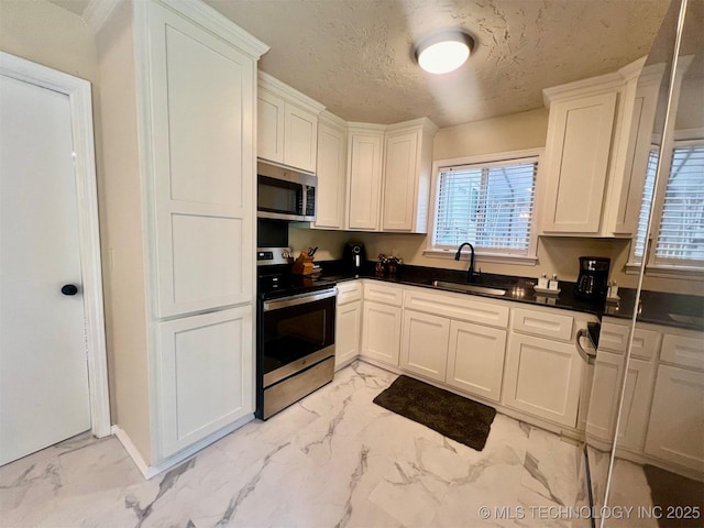 kitchen featuring marble finish floor, a sink, dark countertops, a textured ceiling, and stainless steel appliances