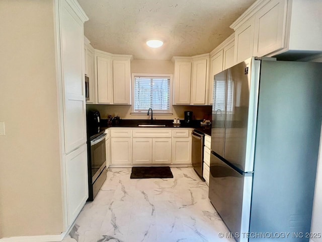 kitchen with a sink, stainless steel appliances, white cabinets, a textured ceiling, and marble finish floor