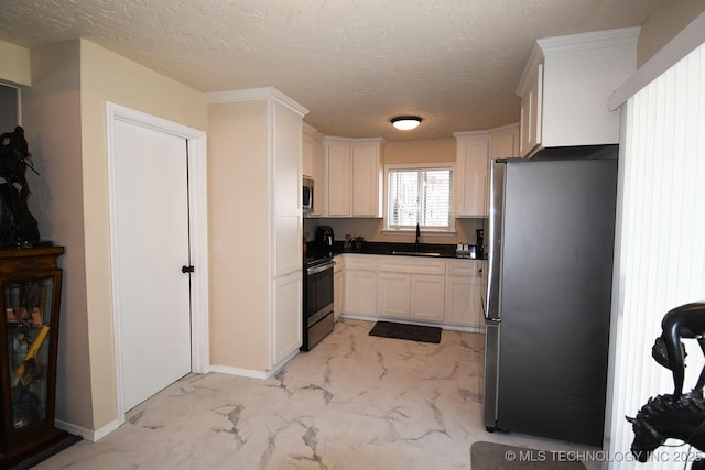 kitchen featuring stainless steel appliances, marble finish floor, a textured ceiling, white cabinetry, and a sink