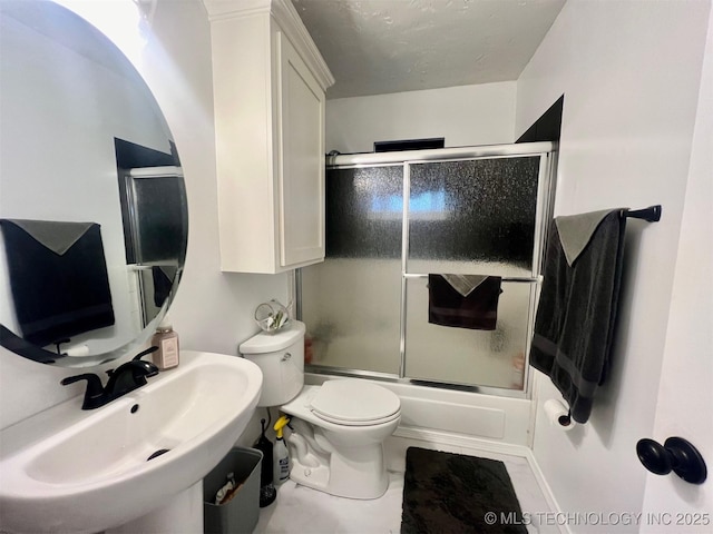 bathroom featuring toilet, shower / bath combination with glass door, and a sink