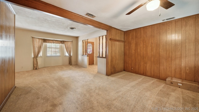 carpeted empty room featuring a ceiling fan, visible vents, and wood walls