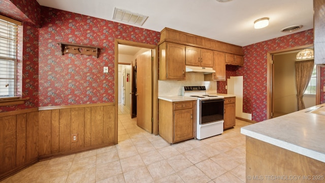 kitchen featuring visible vents, wallpapered walls, under cabinet range hood, a wainscoted wall, and electric range