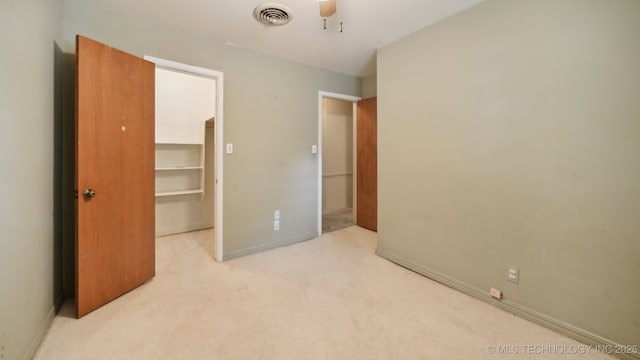 unfurnished bedroom featuring a spacious closet, visible vents, ceiling fan, light carpet, and a closet