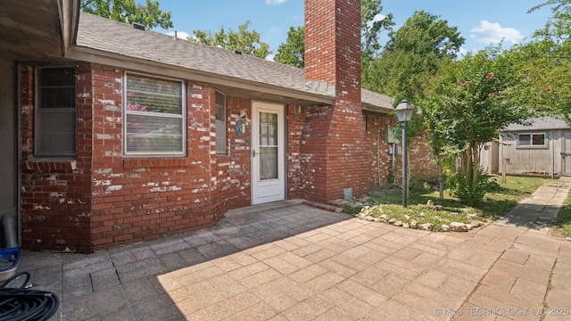 view of exterior entry featuring brick siding, a chimney, and roof with shingles