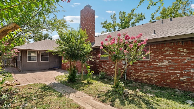 rear view of property with a patio area, brick siding, roof with shingles, and a chimney