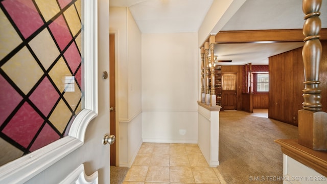 foyer featuring light tile patterned floors, baseboards, light colored carpet, and wooden walls