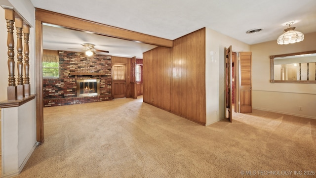 unfurnished living room featuring visible vents, beamed ceiling, carpet, wood walls, and a brick fireplace