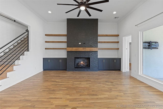 unfurnished living room with crown molding, a brick fireplace, and light wood-type flooring