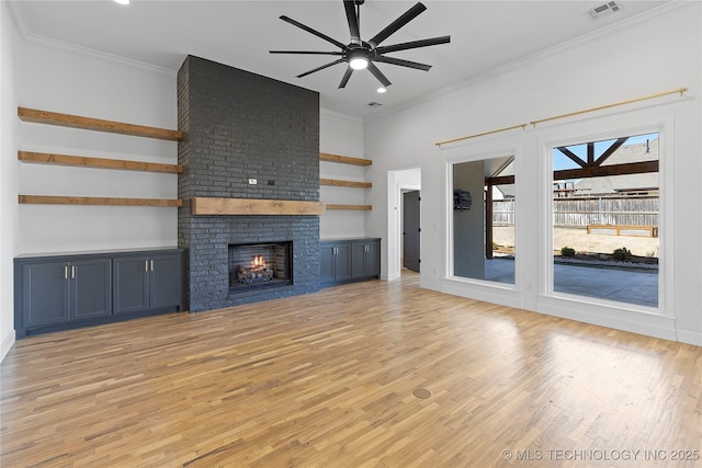 unfurnished living room featuring crown molding, a fireplace, visible vents, and light wood-type flooring