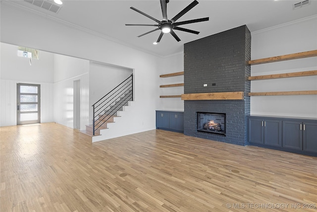 unfurnished living room with visible vents, a brick fireplace, crown molding, stairs, and light wood-style flooring