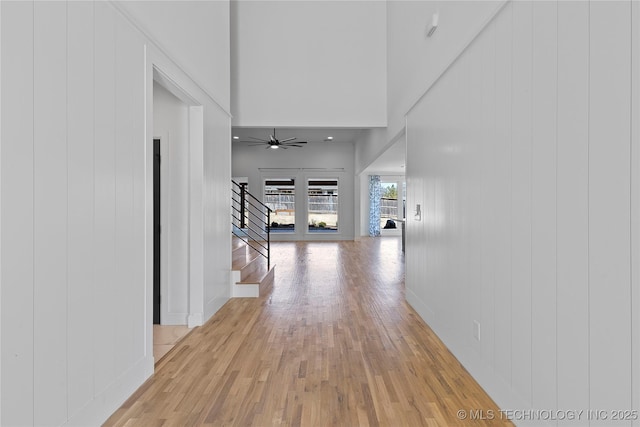 hallway featuring stairway, a towering ceiling, and light wood finished floors