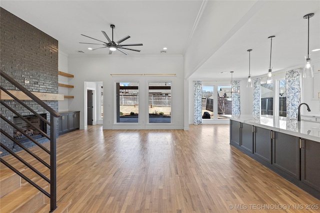 unfurnished living room with baseboards, ornamental molding, light wood-style flooring, a ceiling fan, and a sink