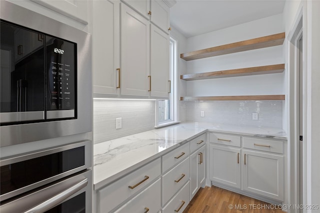 kitchen with light wood finished floors, open shelves, built in microwave, decorative backsplash, and white cabinets