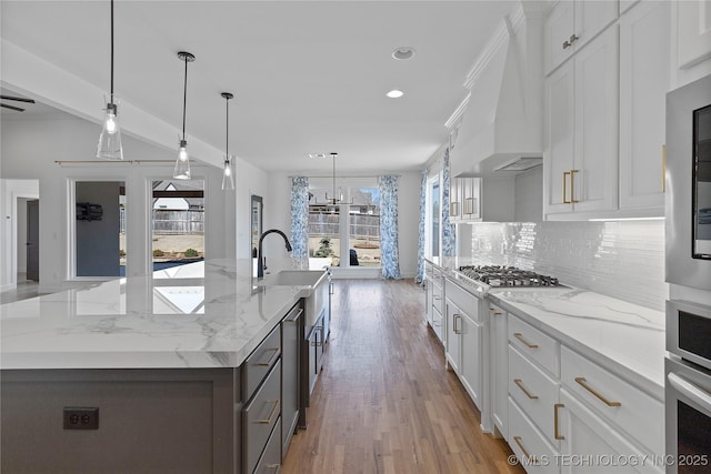 kitchen featuring decorative backsplash, a large island with sink, custom exhaust hood, white cabinetry, and a sink