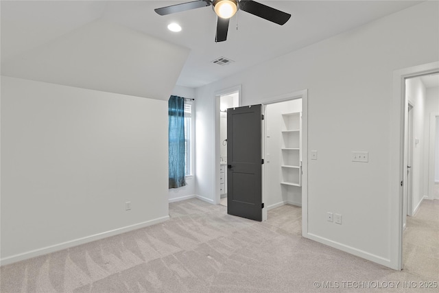 unfurnished bedroom featuring visible vents, a walk in closet, baseboards, light colored carpet, and a ceiling fan