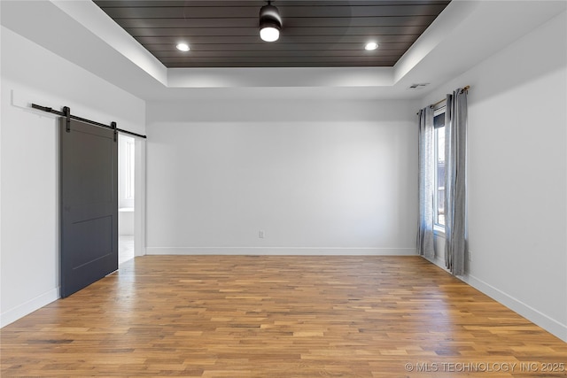 empty room with a barn door, a raised ceiling, baseboards, and light wood finished floors