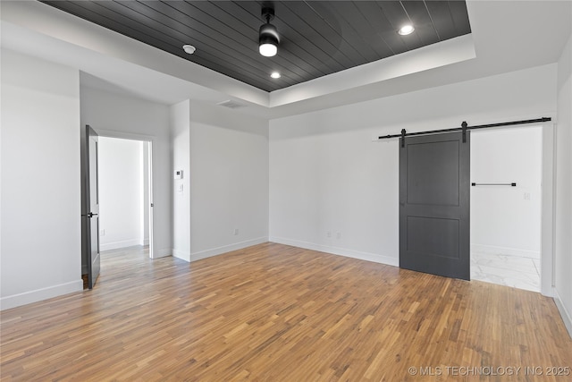 unfurnished room featuring a tray ceiling, a barn door, baseboards, and wooden ceiling