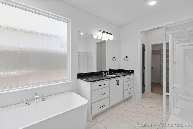 full bath with vanity, a walk in closet, a freestanding tub, and marble finish floor