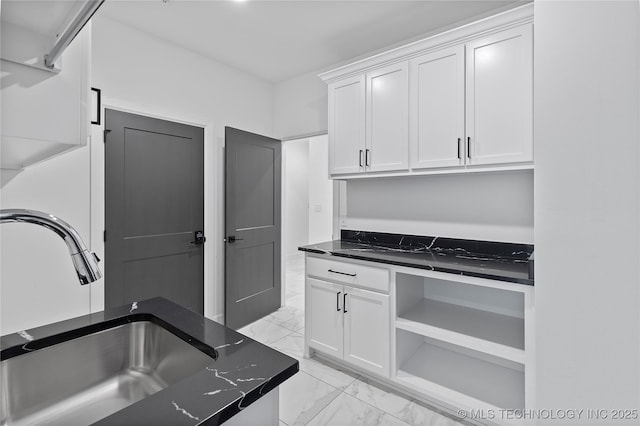 kitchen with a sink, marble finish floor, dark stone countertops, and white cabinetry