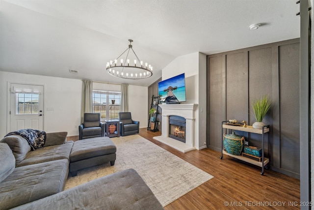 living area featuring wood finished floors, visible vents, an inviting chandelier, a lit fireplace, and vaulted ceiling