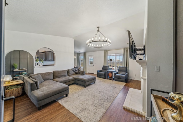 living room featuring a chandelier, arched walkways, wood finished floors, and vaulted ceiling