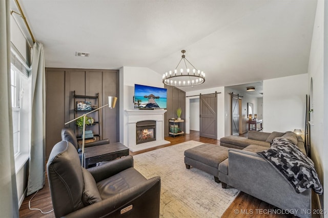 living room featuring a barn door, wood finished floors, visible vents, and lofted ceiling