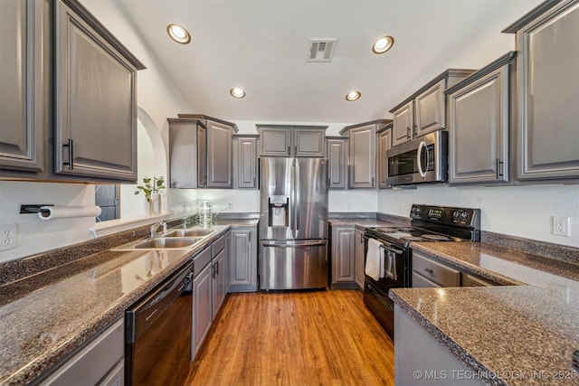 kitchen with visible vents, light wood finished floors, gray cabinetry, a sink, and black appliances