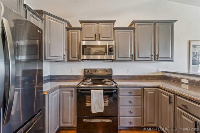 kitchen with stainless steel appliances, lofted ceiling, and dark countertops