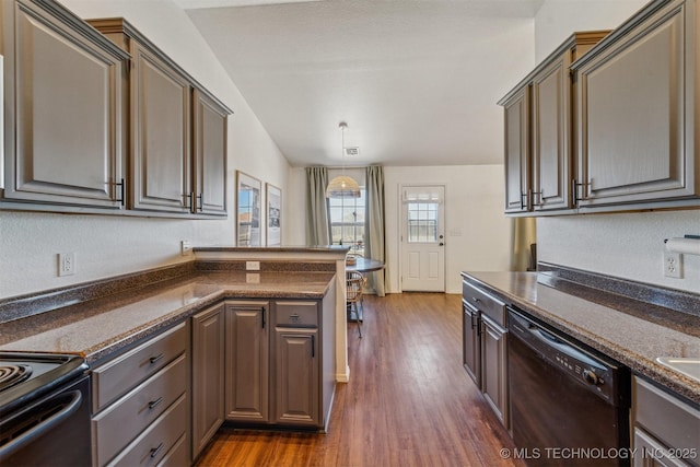 kitchen featuring dark countertops, lofted ceiling, a peninsula, black appliances, and dark wood-style flooring