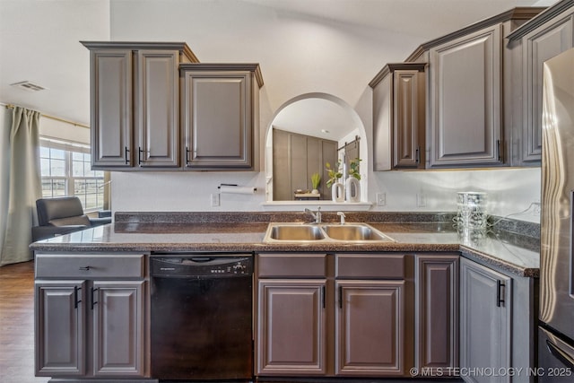 kitchen featuring visible vents, stainless steel refrigerator, a sink, black dishwasher, and dark countertops