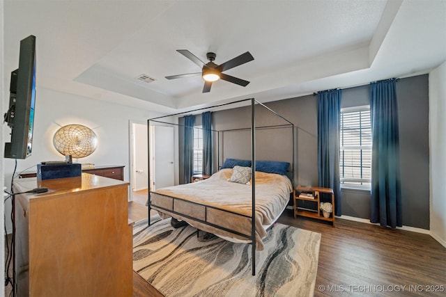 bedroom with a tray ceiling, baseboards, visible vents, and wood finished floors