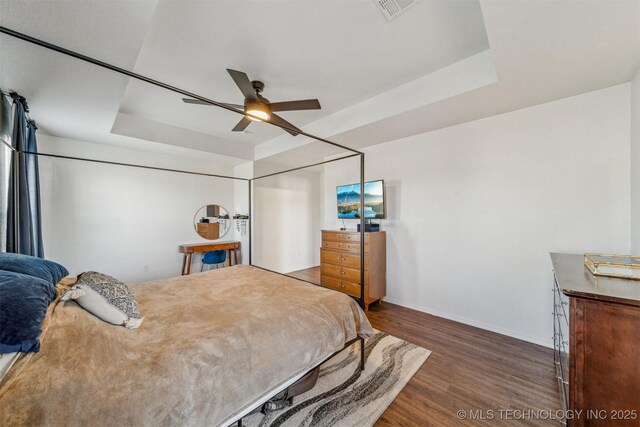 bedroom featuring visible vents, a raised ceiling, a ceiling fan, wood finished floors, and baseboards