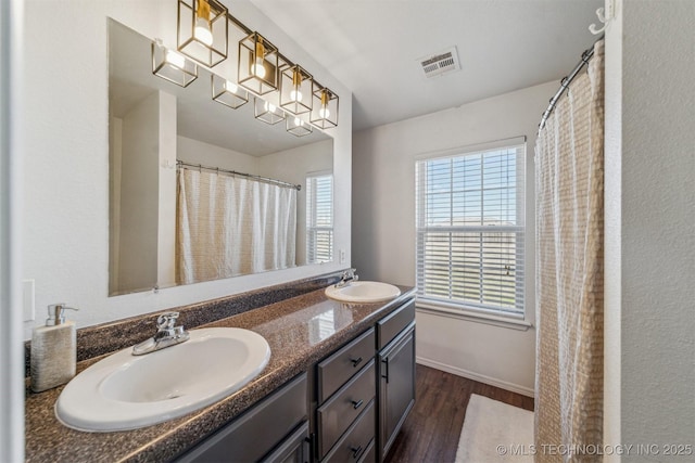 full bathroom with double vanity, visible vents, wood finished floors, and a sink