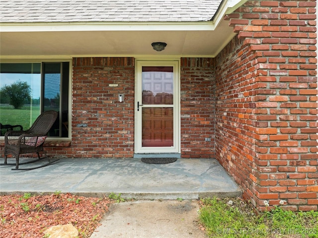 entrance to property with brick siding and roof with shingles