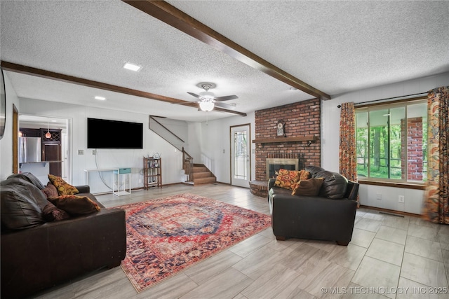 living area with stairway, a ceiling fan, beam ceiling, a textured ceiling, and a brick fireplace