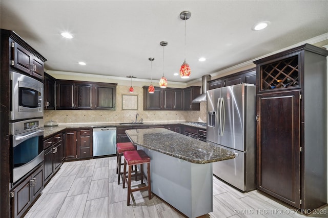 kitchen featuring a sink, a kitchen island, dark stone counters, appliances with stainless steel finishes, and wall chimney exhaust hood