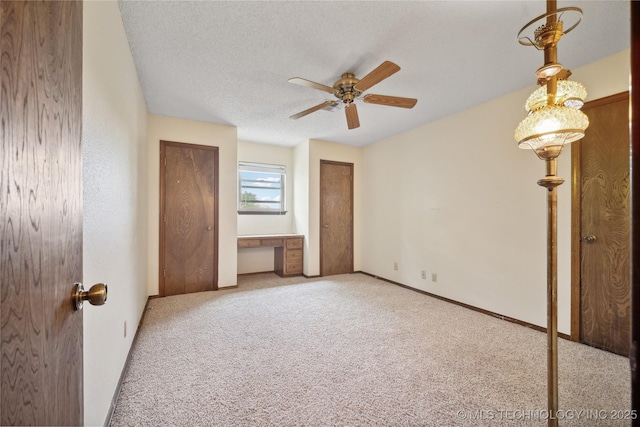 unfurnished bedroom featuring baseboards, carpet, multiple closets, built in desk, and a textured ceiling