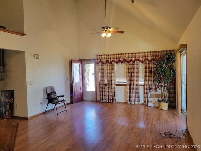 living area featuring ceiling fan, wood finished floors, baseboards, and high vaulted ceiling