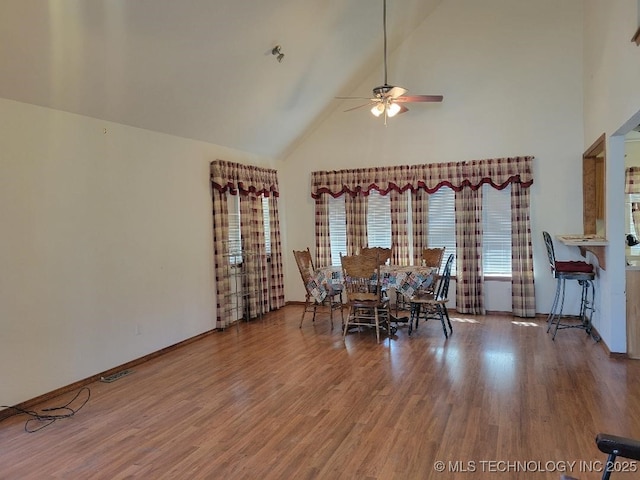 unfurnished dining area featuring baseboards, high vaulted ceiling, ceiling fan, and wood finished floors