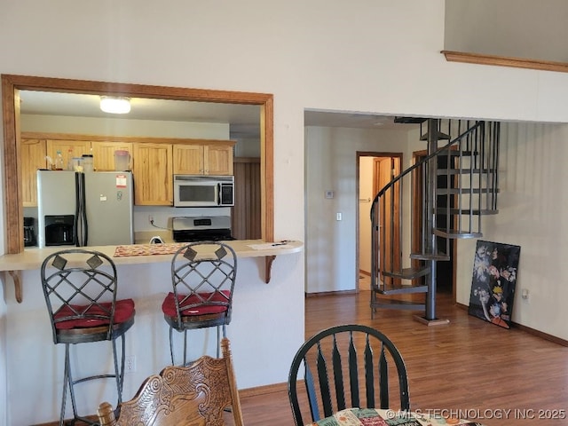 kitchen with dark wood finished floors, a peninsula, stainless steel appliances, and a breakfast bar