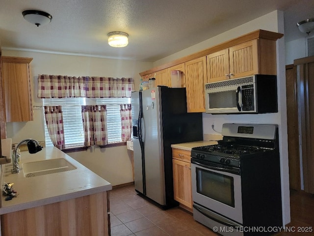 kitchen with light brown cabinetry, light countertops, tile patterned floors, stainless steel appliances, and a sink