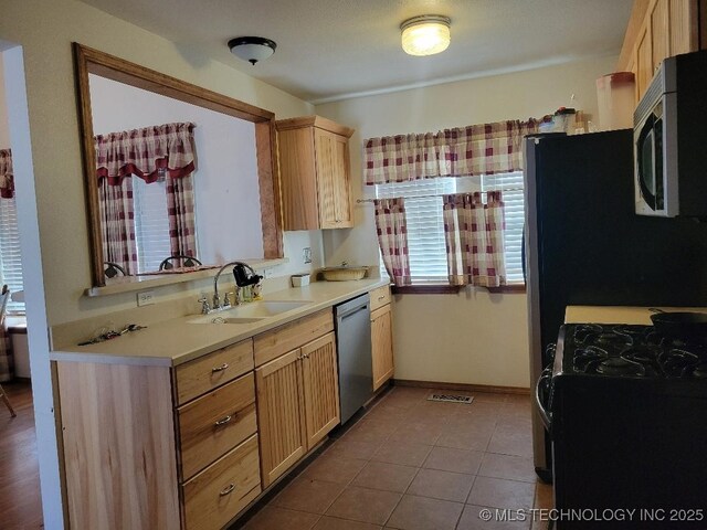 kitchen featuring light brown cabinetry, light countertops, tile patterned floors, stainless steel appliances, and a sink