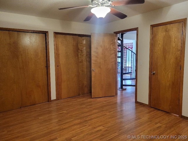 unfurnished bedroom featuring wood finished floors, baseboards, two closets, and ceiling fan