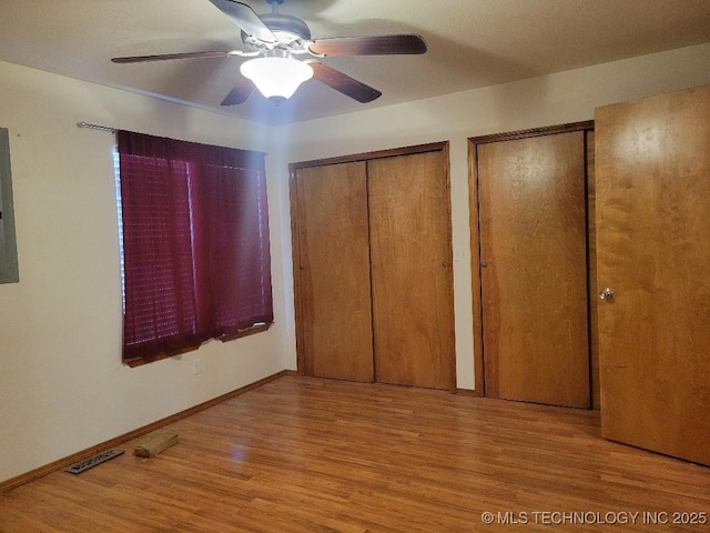 unfurnished bedroom with multiple closets, electric panel, wood finished floors, baseboards, and ceiling fan