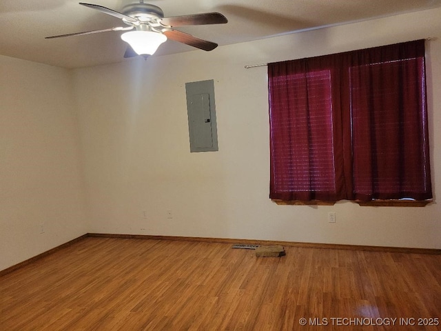 unfurnished room featuring electric panel, a ceiling fan, baseboards, and wood finished floors