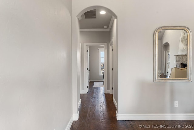 corridor featuring visible vents, crown molding, baseboards, wood finished floors, and arched walkways