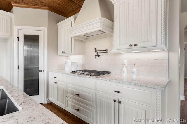 kitchen with custom range hood, light stone counters, backsplash, stainless steel gas stovetop, and white cabinets