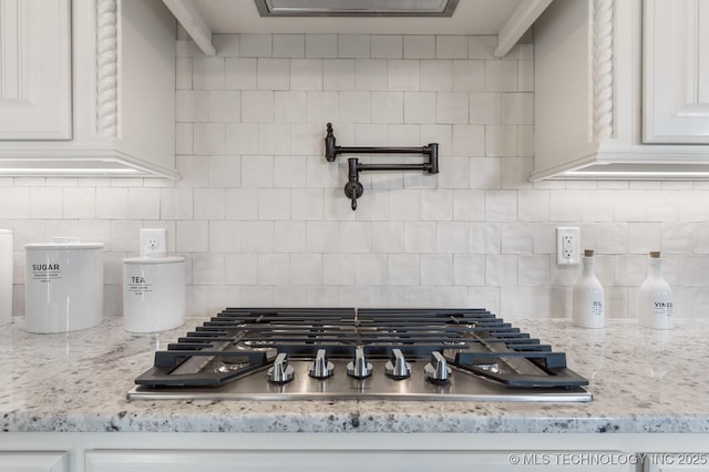 interior details featuring decorative backsplash, light stone countertops, white cabinetry, and stainless steel gas stovetop